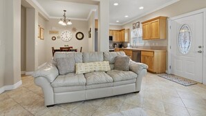 Una sala de estar con un sofá color beige, una mesa de comedor y una cocina al fondo.