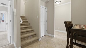 Un pasillo con una escalera alfombrada, un comedor con mesa y sillas, y una puerta blanca.