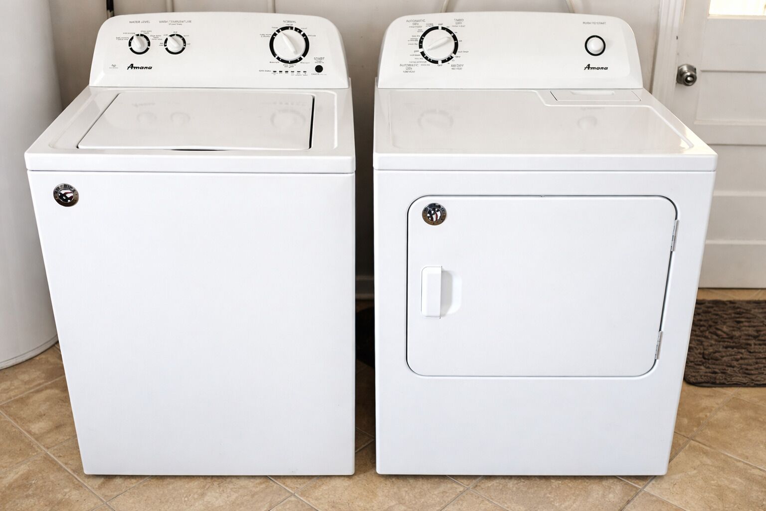 Two white front-loading washing machines with control panels, a door, and a tiled floor.
