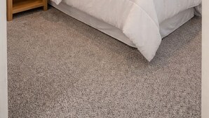 Ein Schlafzimmer mit einem Bett, einem Nachttisch, einer Lampe, einem gerahmten Bild und einem Fenster mit Vorhängen.