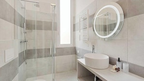 A modern bathroom with a glass-enclosed shower, a round mirror, and a white sink.