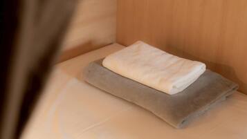 A neatly made bed with a folded white towel and a gray blanket.