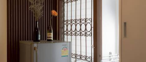 A compact kitchen with a refrigerator, a wooden panel wall, and a window with decorative metal bars.