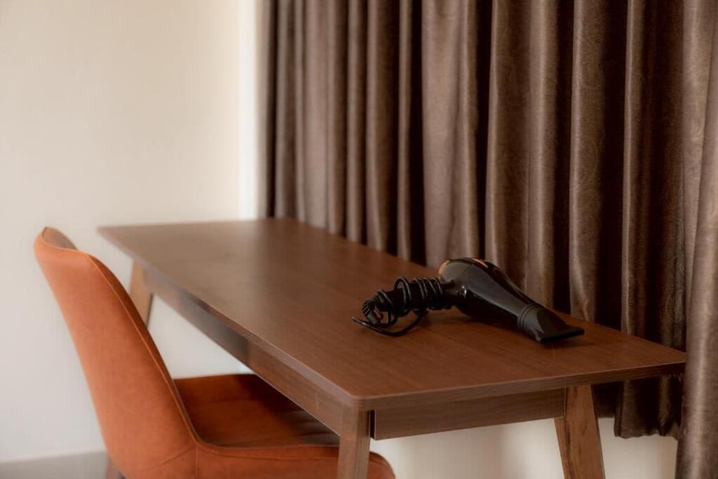 A wooden dining table with a black object on it, a brown curtain in the background, and an orange chair in front.