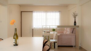 Una habitación moderna y luminosa con una mesa de comedor, sillas, un sofá, una estantería y una ventana con cortinas translúcidas.