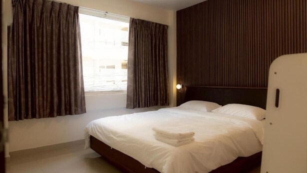 Una habitación de hotel con cama, cortinas, cabecera y ventana.