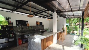 A modern kitchen with a marble island, wooden stools, and a view of the surrounding greenery. - Basilia Guest House - 1 BDR with bathroom (Santa Fe)