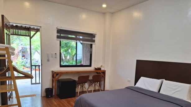 A bedroom with a bed, a desk, two chairs, a window, and a wooden staircase. - Basilia Guest House - 1 BDR with bathroom (Santa Fe)