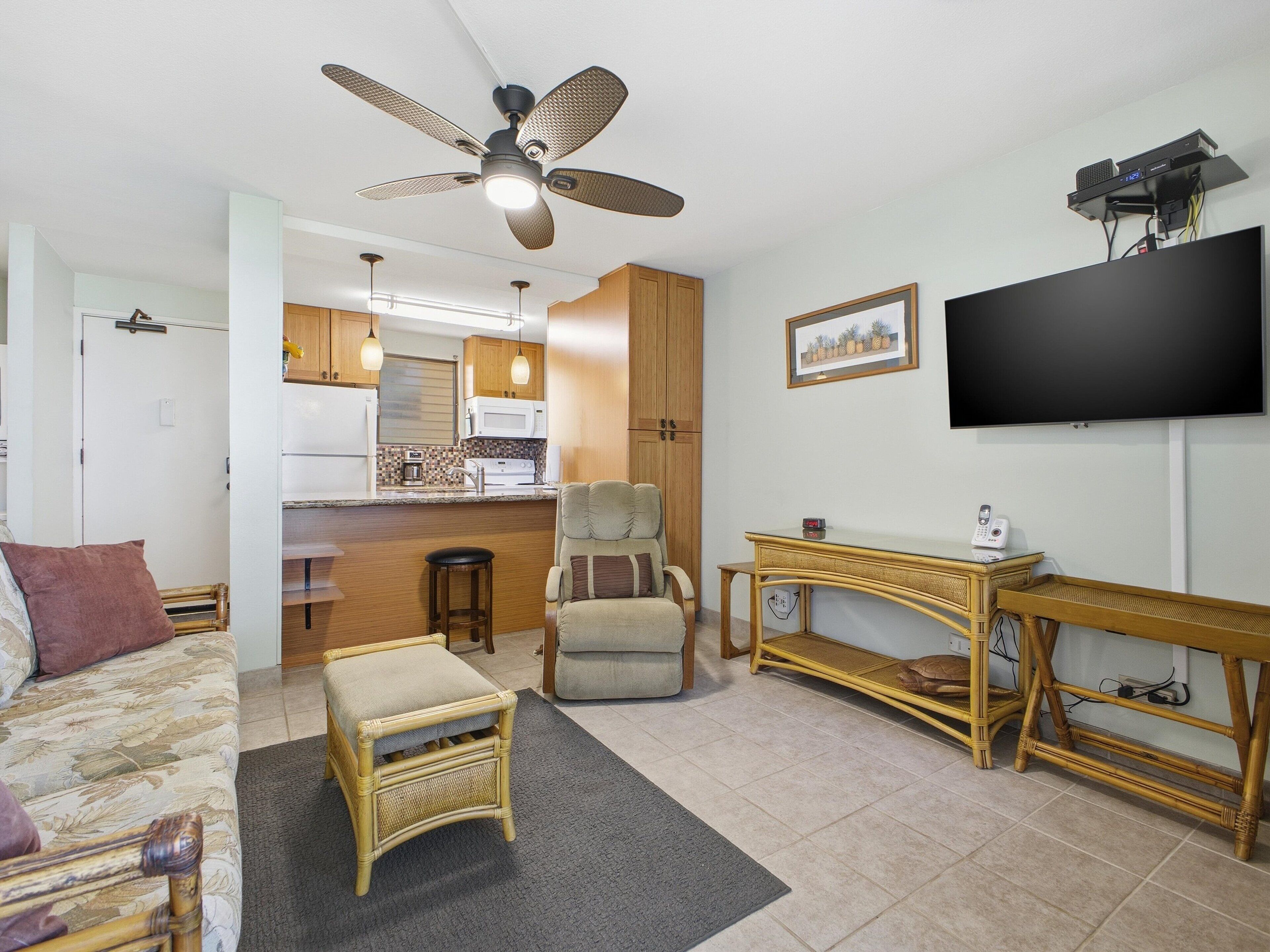 Un espacio habitable compacto con kitchenette, comedor y zona de estar con sofá y sillones.