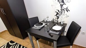 Una mesa de comedor dispuesta con platos, cubiertos y vasos, bordeada por sillas negras, en una habitación con suelo de baldosas y alfombra estampada de cebra.