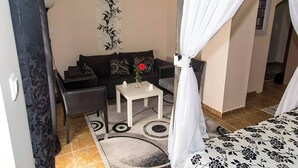 Una habitación con un sofá negro, una mesa blanca con un jarrón y una alfombra estampada.