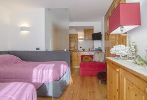 Ein kleines Zimmer mit einem Bett, einem roten Sofa, einem Holzschrank und einem Fernseher.