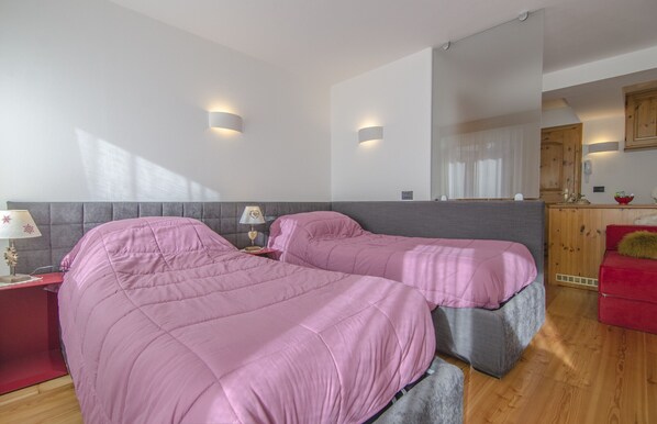 Ein Schlafzimmer mit zwei Betten, einem roten Nachttisch, einer Lampe und einem Holzschrank.