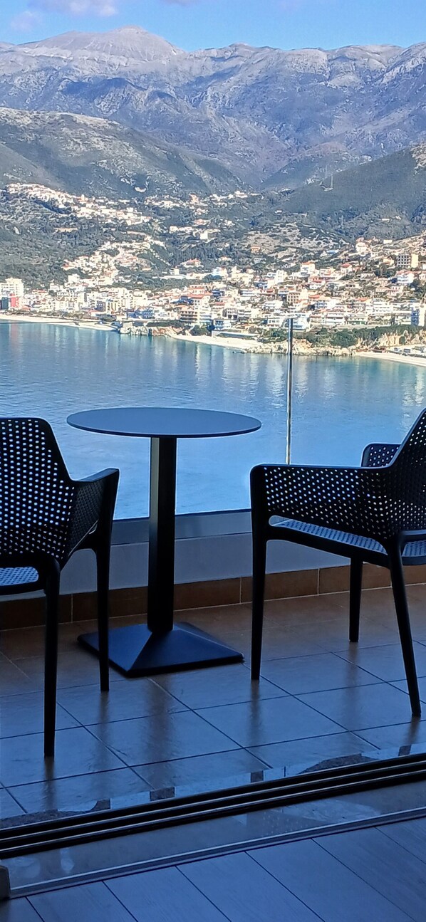Una terrazza con due sedie e un tavolo, affacciata su una località costiera e montagne.