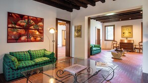 A spacious room with a green patterned sofa, a glass coffee table, and a piano in the background. - Il Salice B&B Country Luxury (Due Carrare)