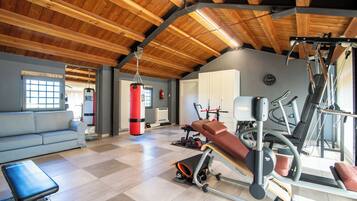 Un gimnasio amplio con diversos equipos de ejercicio, un sofá azul y techo de madera.