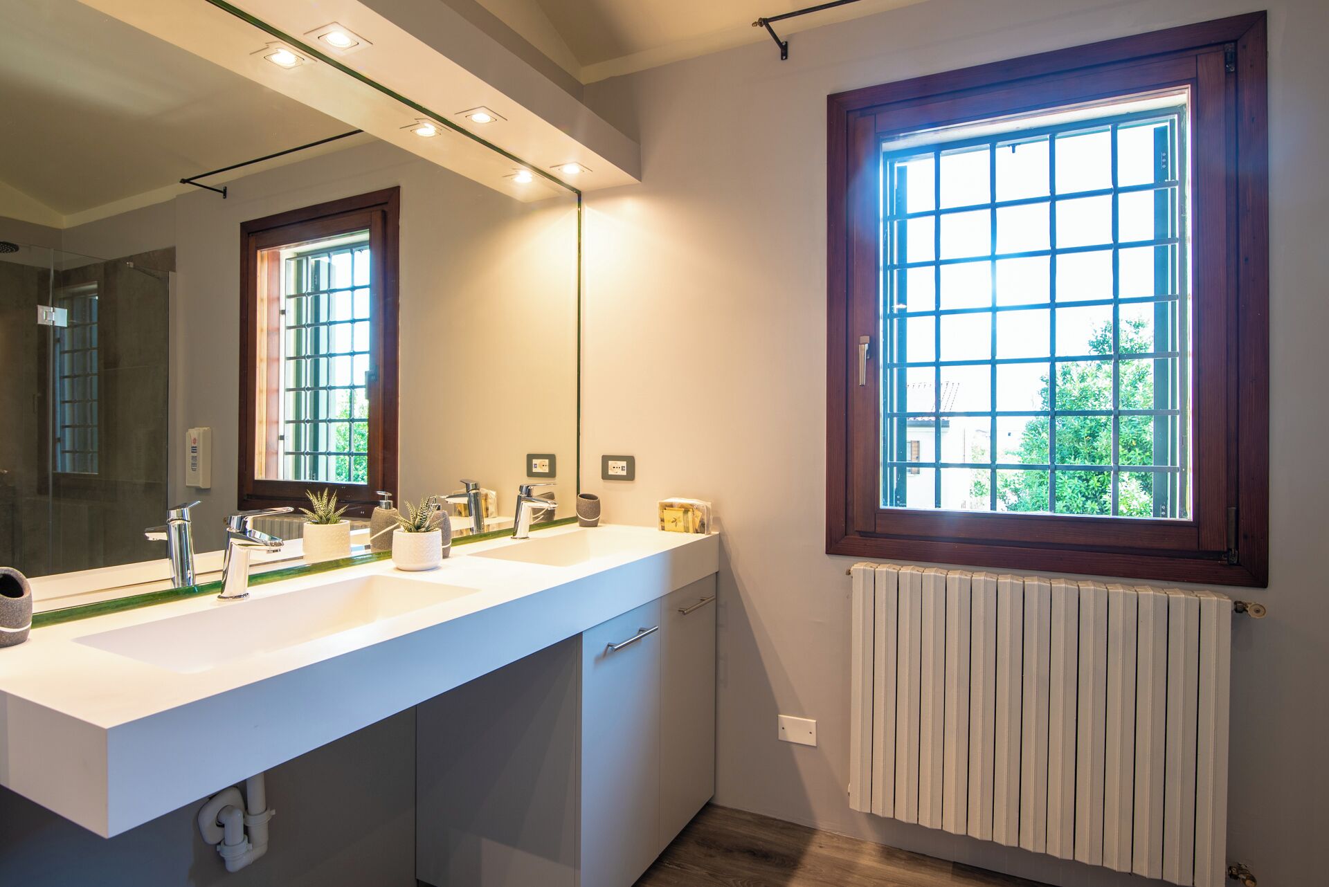 Ein modernes Badezimmer mit einem Doppelwaschbecken, einem großen Spiegel und einem Fenster mit Gittermuster.