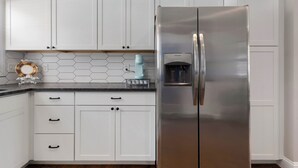 Et køkken med hvide skabe, en rustfris stål køleskab, en backsplash med sekskantede fliser og en lille dekorativ tallerken på bordet.