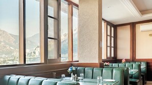 A restaurant with green booths and tables, large windows with a mountain view, and a textured wall. - The Himalayan Residency (Rampur)