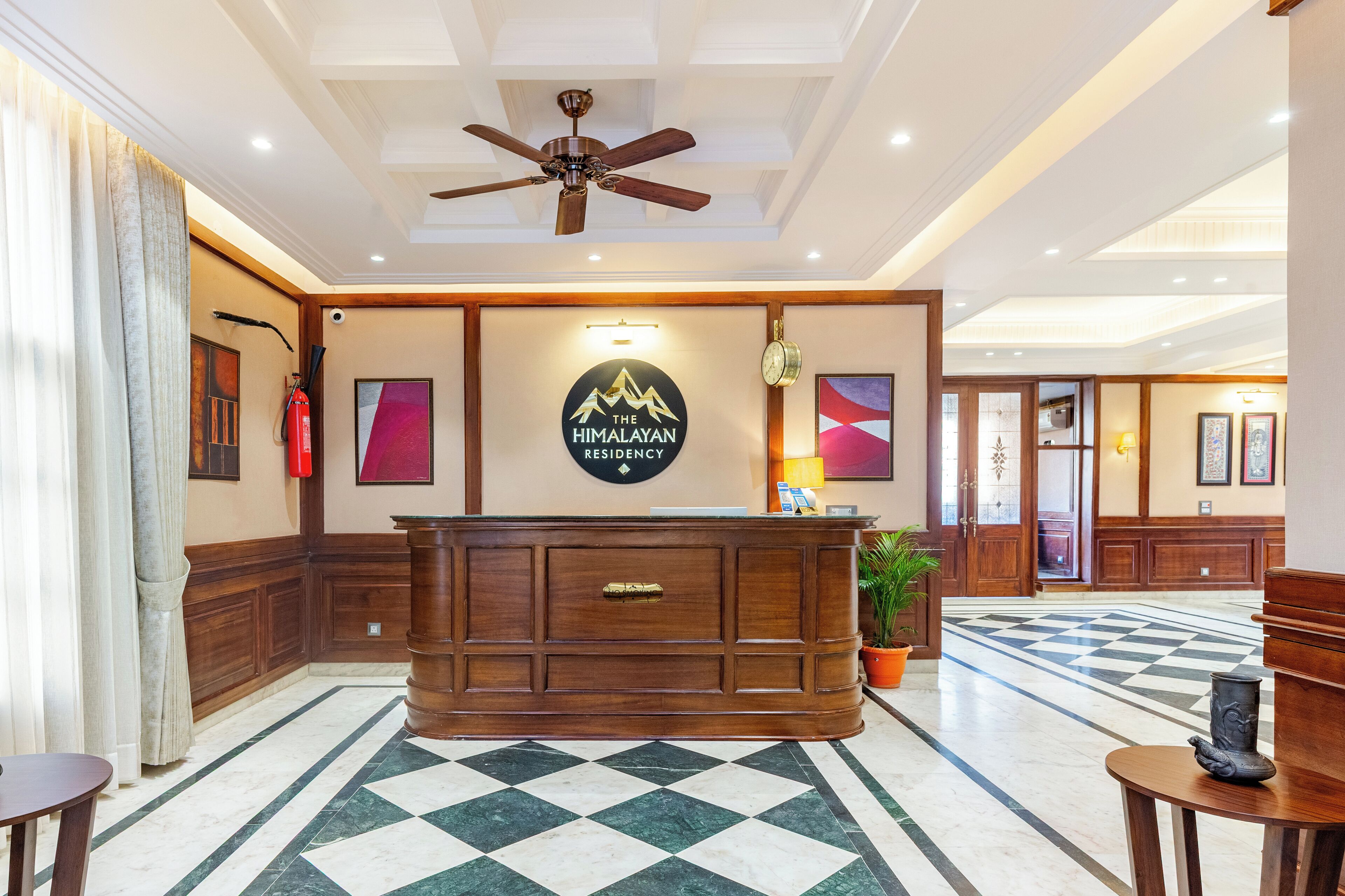 A reception area with a checkered marble floor, a wooden reception desk, a ceiling fan, and a sign that reads "The Himalayan Residency".