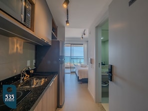 A modern kitchen with a built-in oven, a dining area with a table and chairs, and a bedroom with a bed and a view of the ocean. - Ocean view on 13th floor in Rio Vermelho (Salvador)