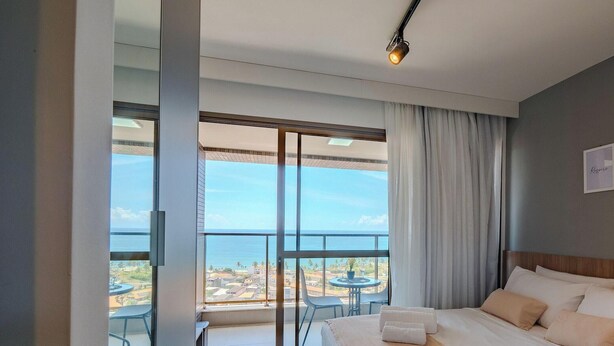 Habitación de hotel con un balcón amplio, una cama con almohadas, una mesita pequeña y una silla.