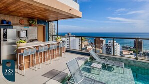 Un bar moderno en la azotea con piscina, taburetes y vistas al océano.