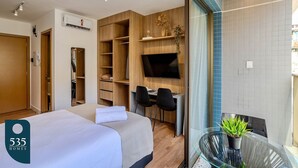 Habitación de hotel con cama, escritorio con dos sillas, televisión y una mesa de vidrio con una planta.