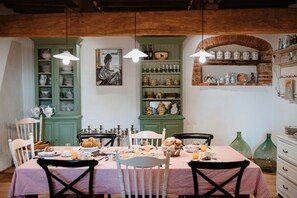 Un comedor con mantel a cuadros, sillas de madera y un aparador verde con vajilla.