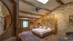 Ein Schlafzimmer mit Steinwand, einem Bett, Holzboden und einem Oberlicht.