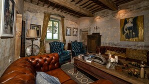 Ein rustikaler Raum mit einem Ledersofa, blauen Sesseln, einem Holztisch und einem Gemälde an der Wand.