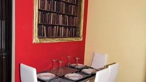 Un comedor con pared roja, una estantería y una mesa preparada para cuatro personas.