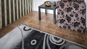 Una sala con cortina estampada, una estantería, un sofá, una mesita y una alfombra.