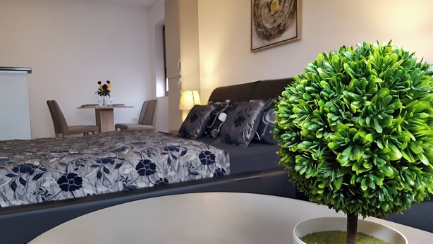Un dormitorio moderno con una cama bien hecha, una mesita con un jarrón de flores y una planta en maceta.