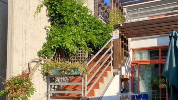 A residential property with a concrete staircase leading to a wooden deck, a small garden with red flowers, and a clear blue sky. - Spacious house separate entrance, private garden pool and close to the sea (Lido di Jesolo)
