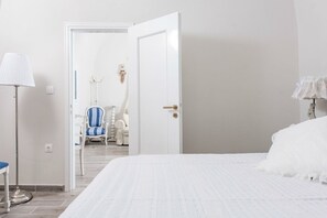 A hotel room with a large bed, a chair, and a lamp. - Villa Iokasti (Santorini)