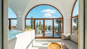 A spacious balcony with a pool, a wooden table, and a sofa. - Leon Villa (Santorini)