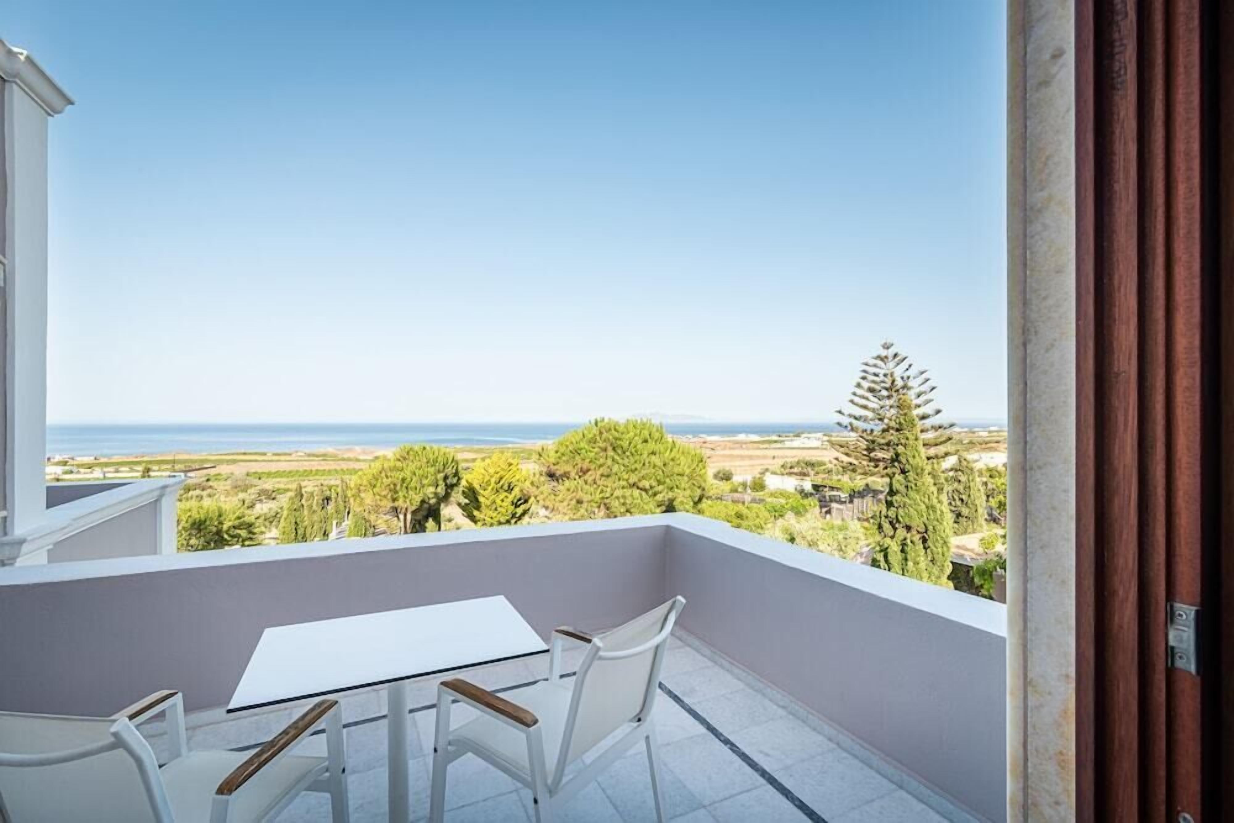 A balcony with a table and chairs, overlooking a coastal landscape.