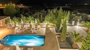 A rooftop pool area with lounge chairs and umbrellas, surrounded by potted plants and trees. - Leon Villa (Santorini)