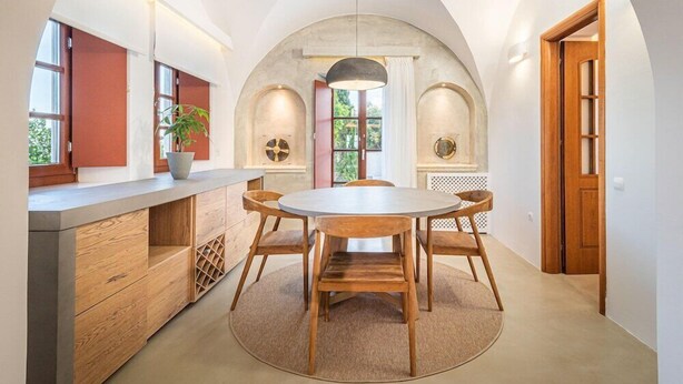 A dining area with a round table and four chairs, a wooden counter with drawers, and a potted plant. - Leon Villa (Santorini)