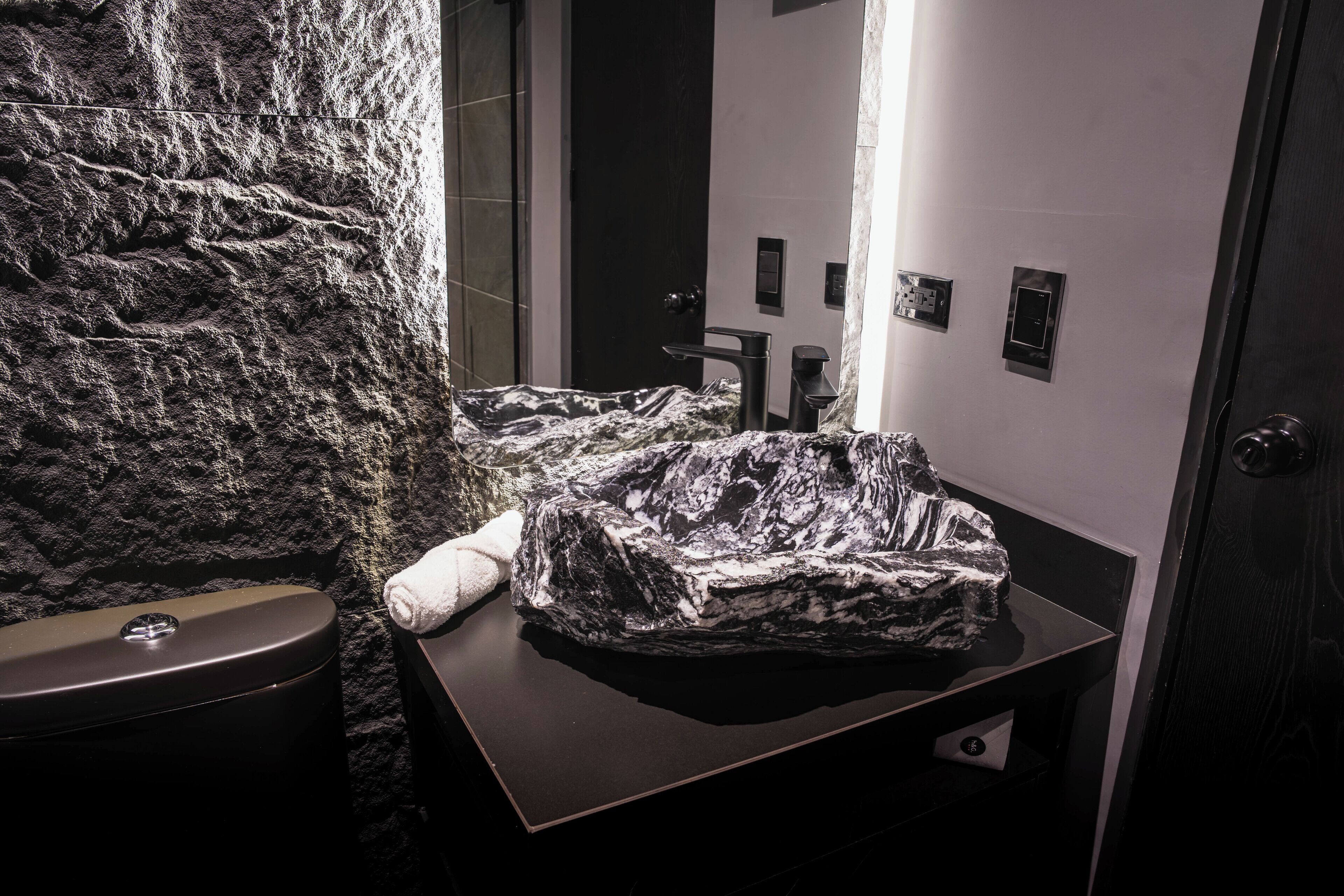 A bathroom with a stone wall, a toilet, a sink, and a mirror.