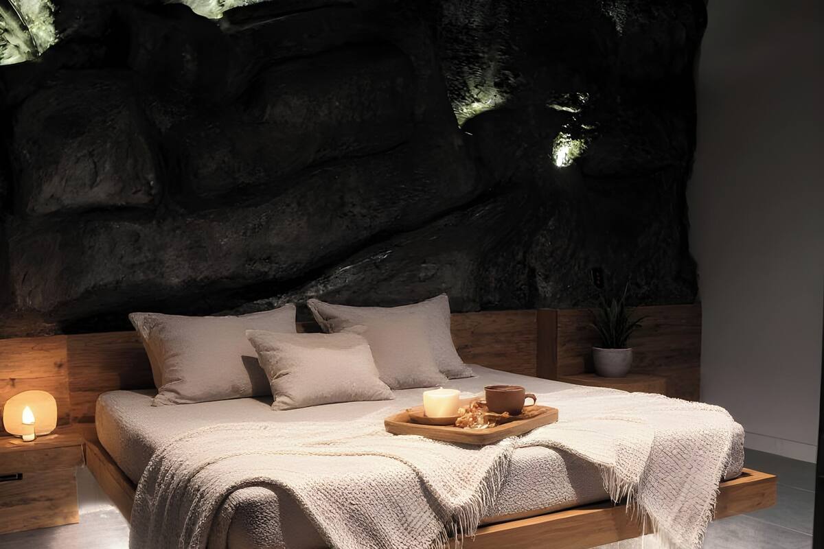 A modern bedroom with a bed, wooden headboard, bedside table, and a wall with a rock-like texture.