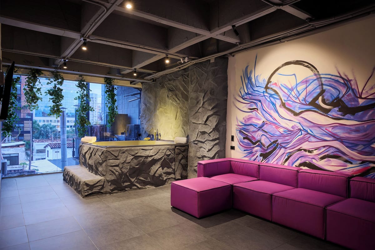 A modern interior with a stone wall, a colorful abstract mural, a pink sectional sofa, and a reception area with a counter and plants.