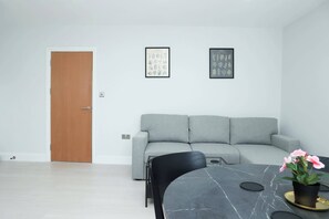 Een moderne woonkamer met een grijze bank, een eettafel met stoelen en een houten deur.
