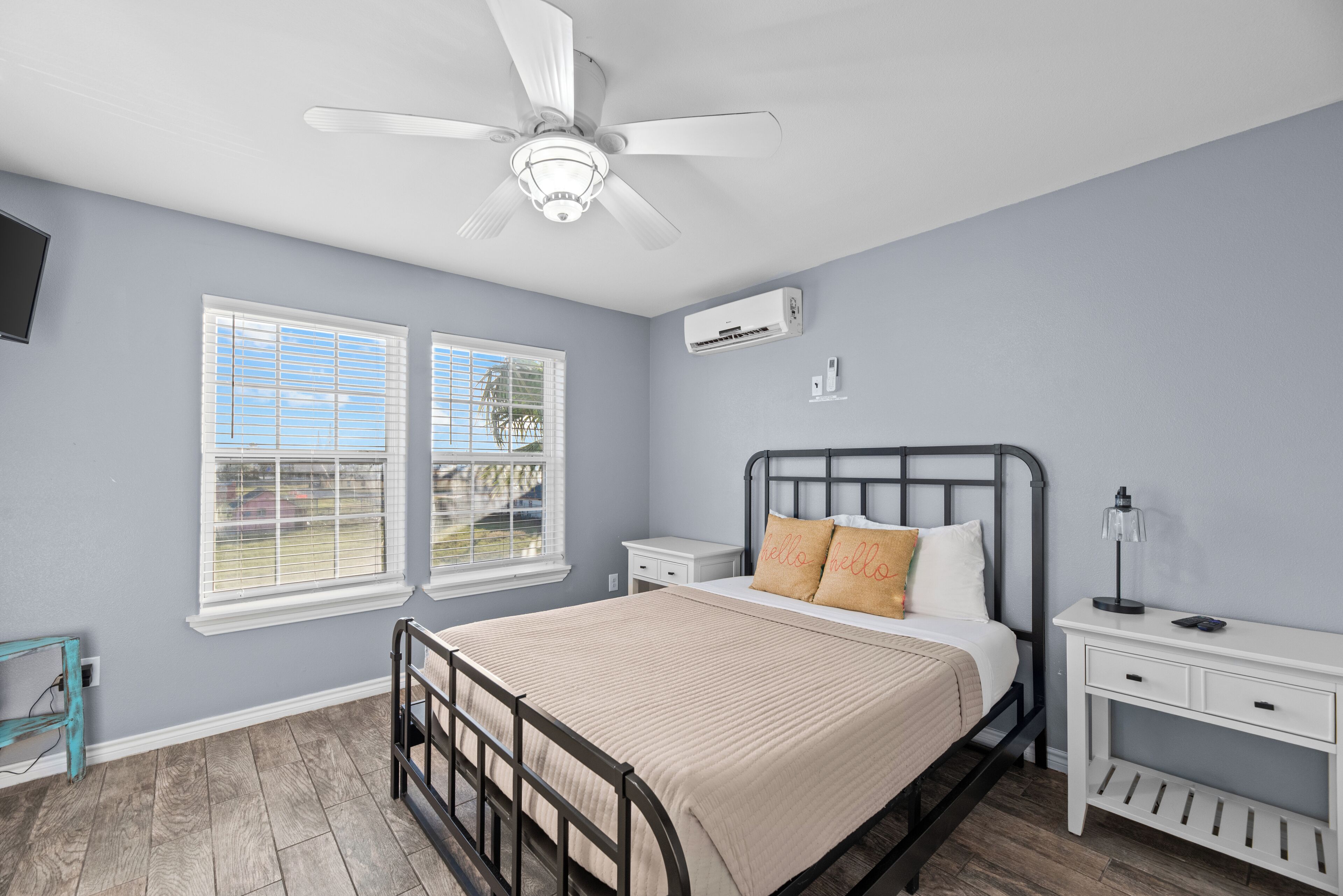 A bedroom with a bed, nightstands, a desk, a ceiling fan, and an air conditioning unit.