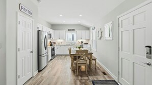 Una cocina moderna con armarios blancos, una isla central y un comedor con mesa y sillas de madera.