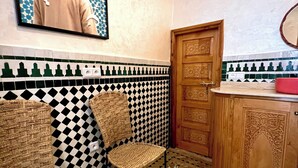 A cozy room with a checkered floor, a woven sofa, a small table with a tissue box, and a wooden door.