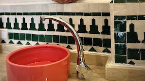 A bathroom with a round mirror, a red basin, and a tiled backsplash.