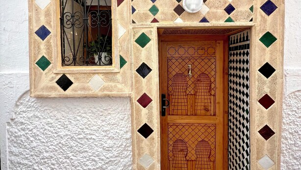 A building with a tiled entrance, a numbered door, and a window with a metal gate.