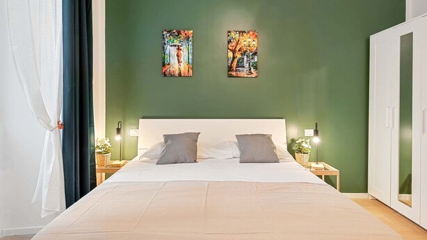 A bedroom with a large bed, two wall-mounted paintings, a white headboard, bedside tables with lamps, and a green wall. - Welcome to 5 Terre Central, a newly renovated guest house located in the heart of La Spezia. Our property is the ideal starting point for those who want to explore the wonders of the Cinque Terre, easily reachable thanks to the proximity of the train sta (La Spezia)